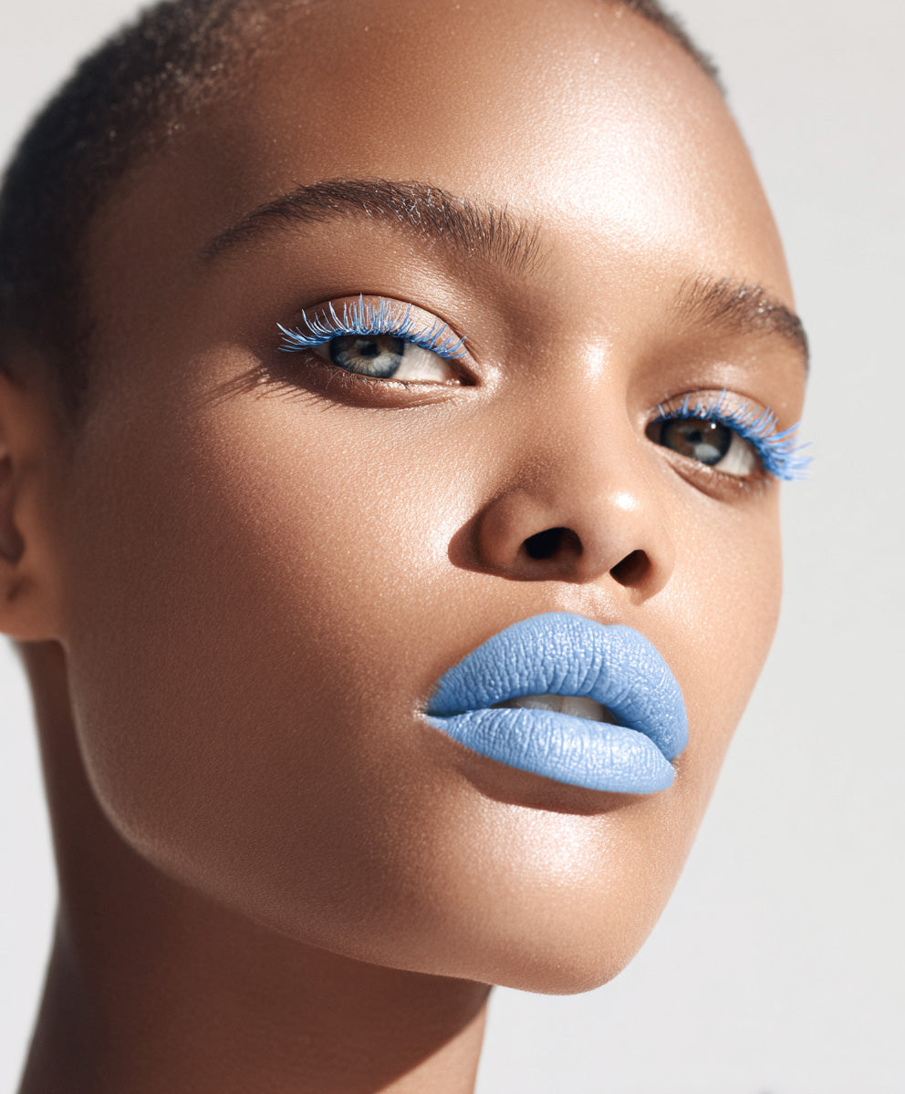 Close-up beauty portrait of a woman wearing bold blue lipstick and matching blue eyelashes.
