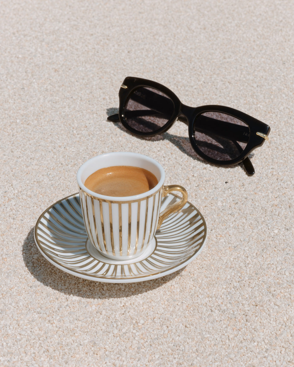 Espresso coffee in striped gold cup with sunglasses on sand, summer lifestyle stock photo