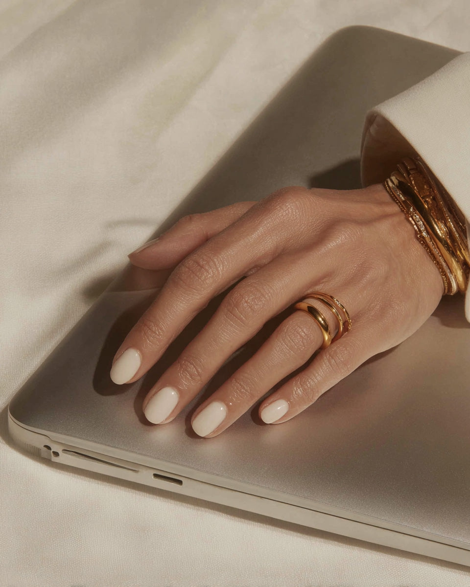 Female hand with neutral manicure and gold jewelry resting on laptop, luxury lifestyle stock photo