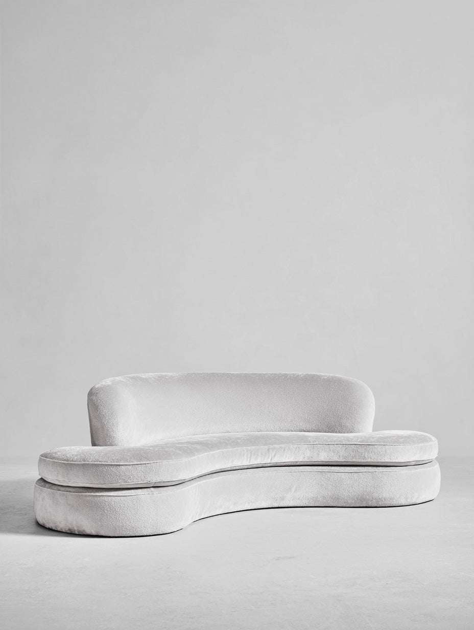 Contemporary curved white sofa in boucle fabric set against a neutral gray background.