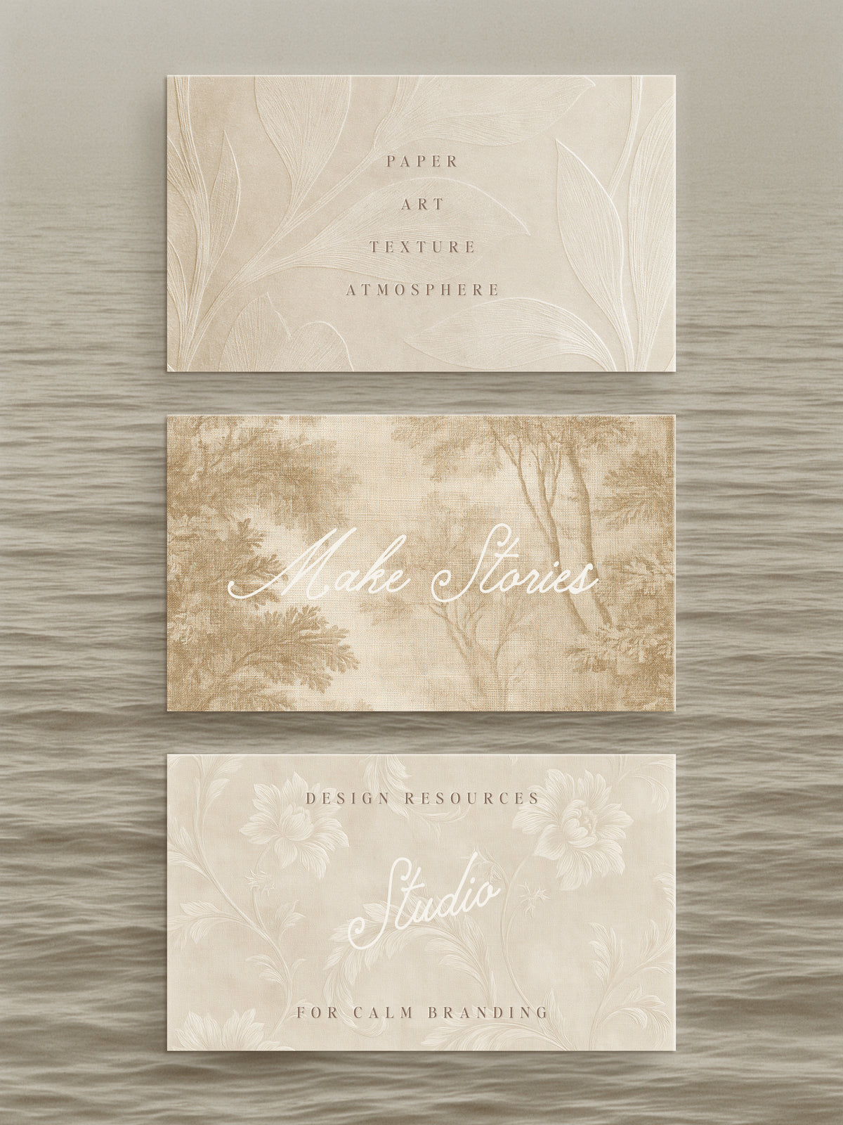 Three rectangular paper cards with a soft beige and cream botanical design are arranged vertically on a textured gray background. The top card reads 'PAPER ART TEXTURE ATMOSPHERE,' the middle reads 'Make Stories,' and the bottom reads 'DESIGN RESOURCES Studio FOR CALM BRANDING.